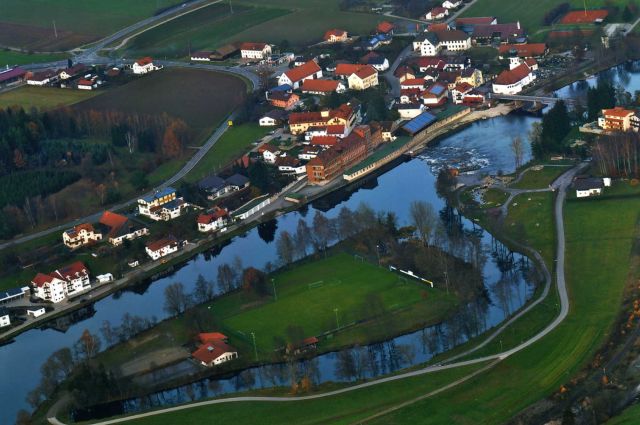 Luftbildaufnahme der Sportanlage des FC Chamerau, die vom Fluss Regen umgeben ist. Im Anschluss Richtung Ortskern erstreckt sich widerum die gemeindliche Parkanlage.jpg